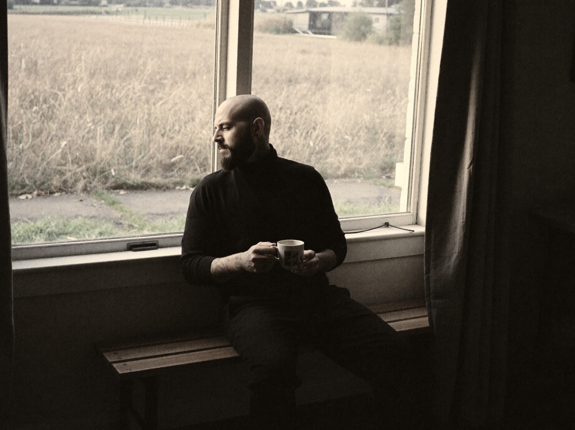 Nicolás Morin by a window with a mug, the farm field outside.