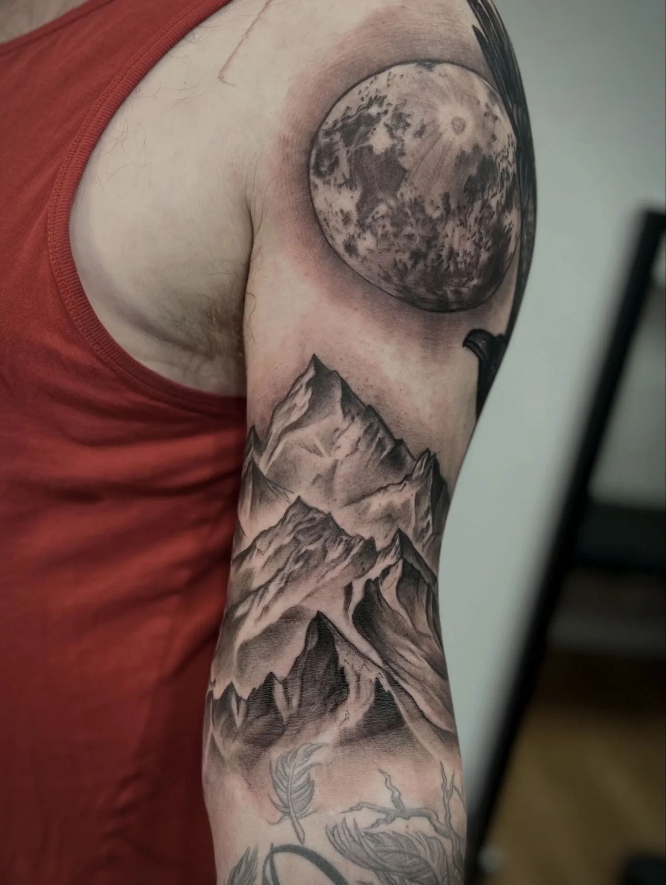 A full moon above a mountain range, running from shoulder to elbow in soft black and grey.