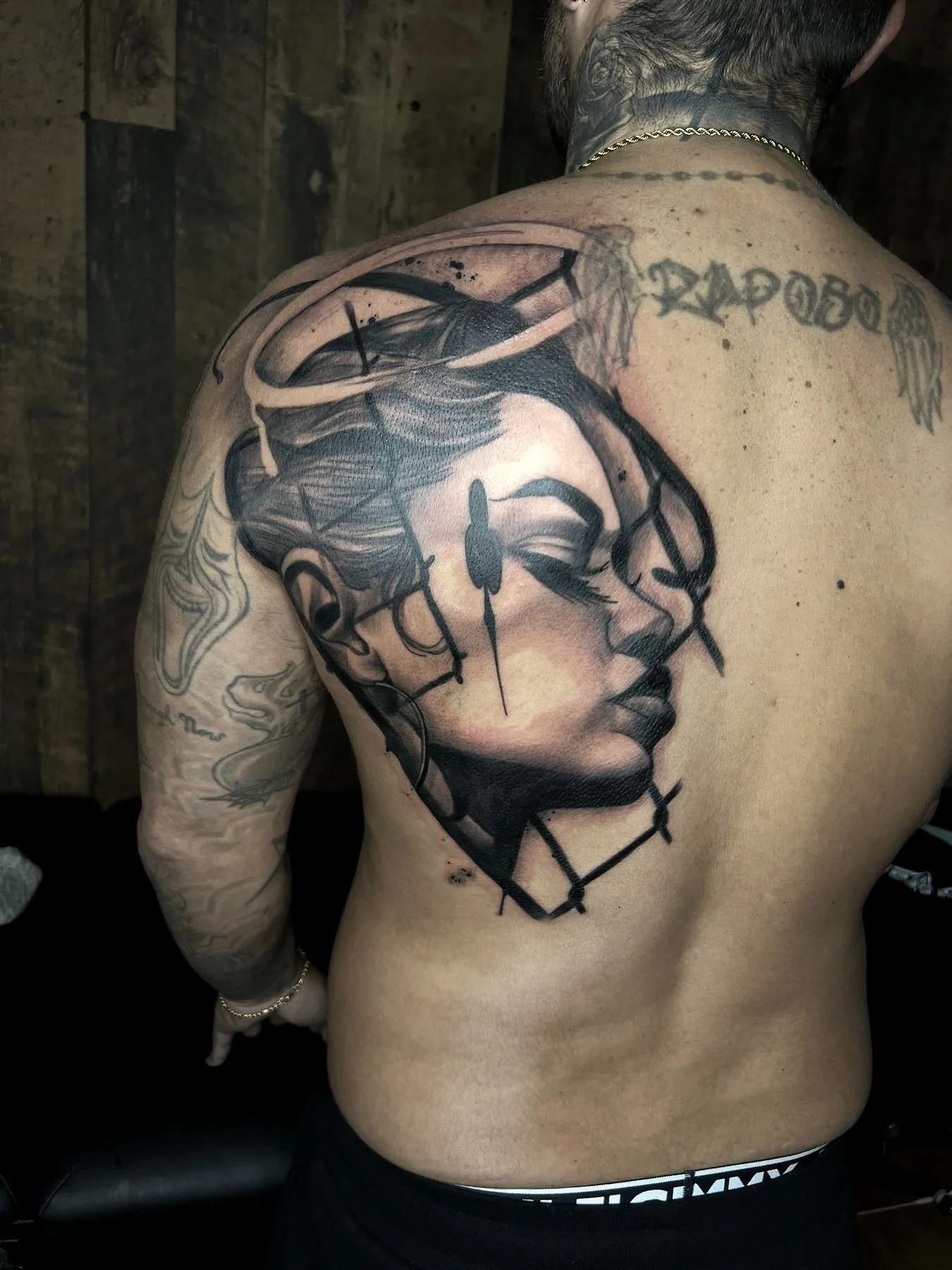 A woman's face broken into geometric planes, tattooed across a back with fine linework and smoke.