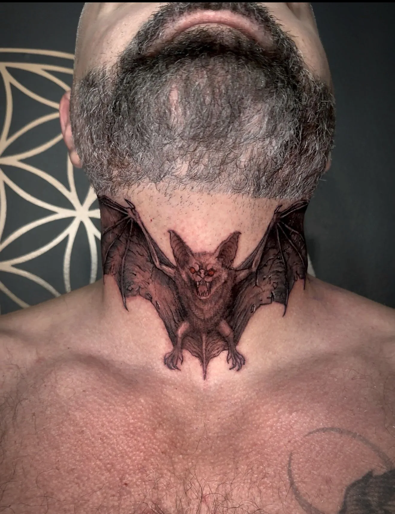 A bat with outstretched wings tattooed across the front of a throat.