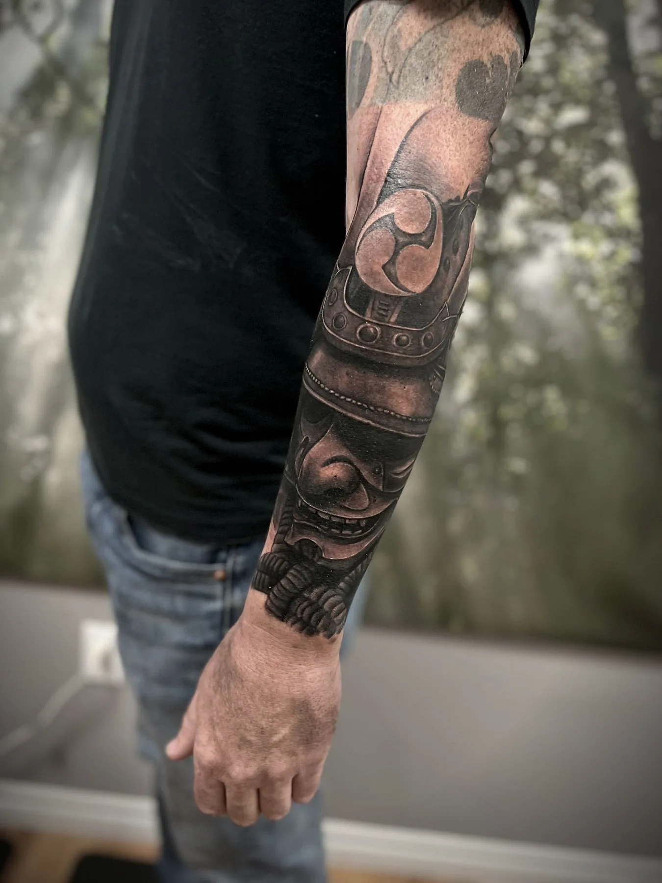 A Japanese sleeve in black and grey: masks, waves and ornament running the length of an arm.