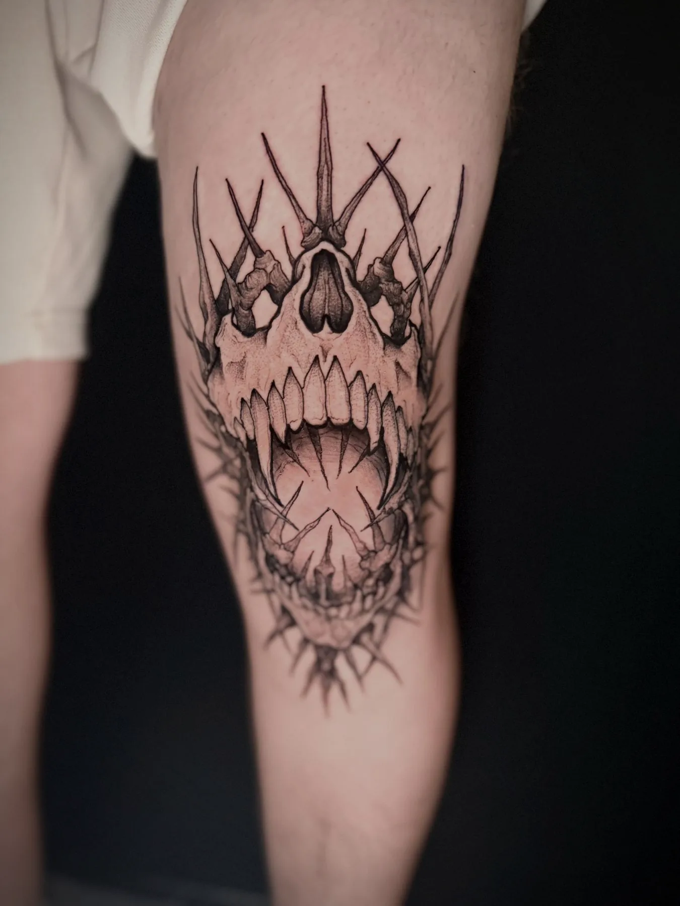 A fanged skull crowned with thorns, tattooed above a knee in fine black linework.