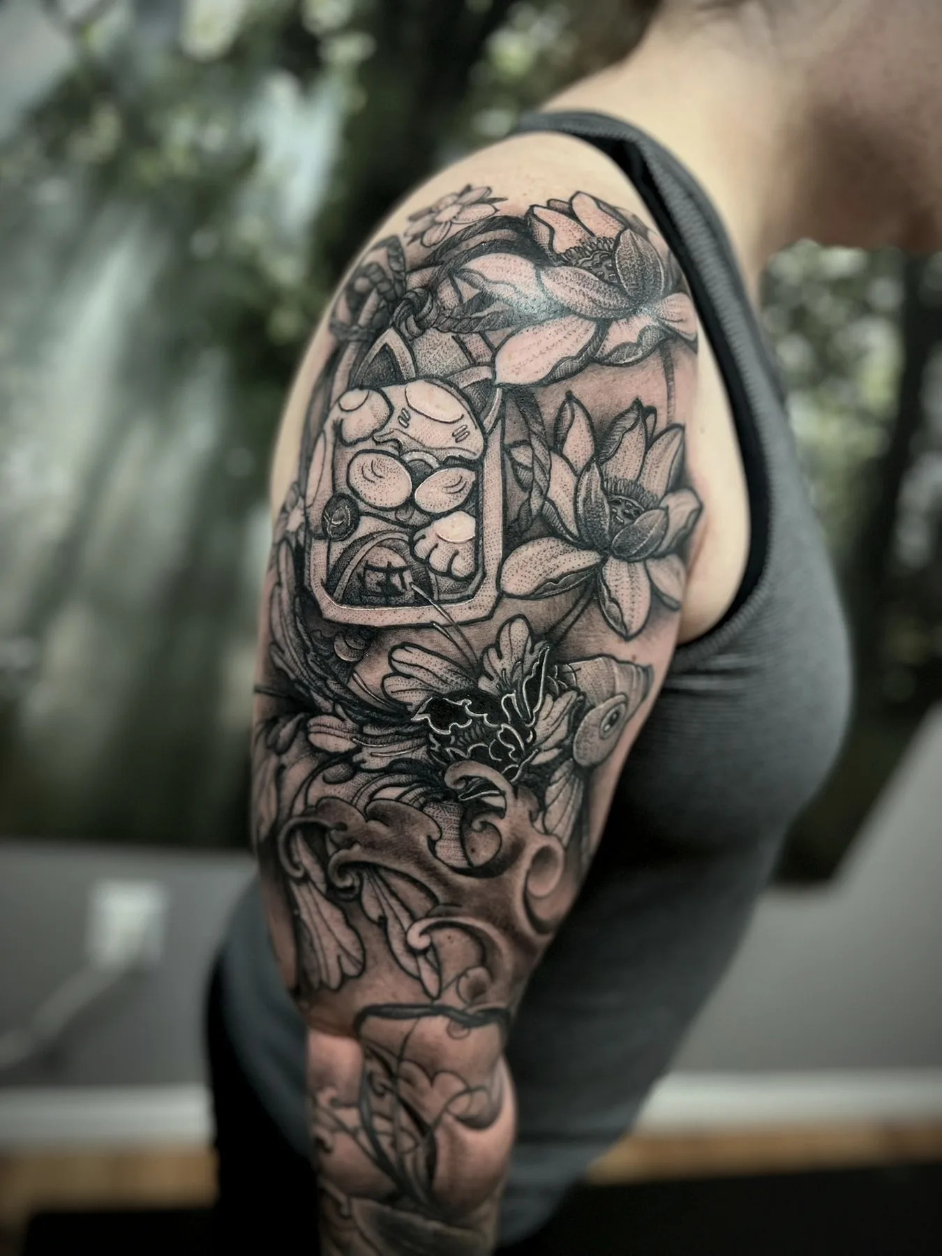 A Japanese floral sleeve in black and grey, lotus and ornament wrapping an upper arm.