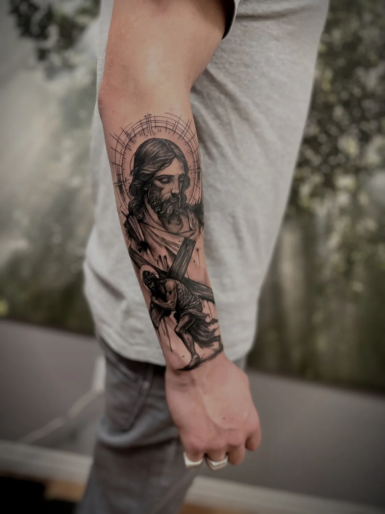 Christ carrying the cross, tattooed along a forearm beneath a fine halo of rays.