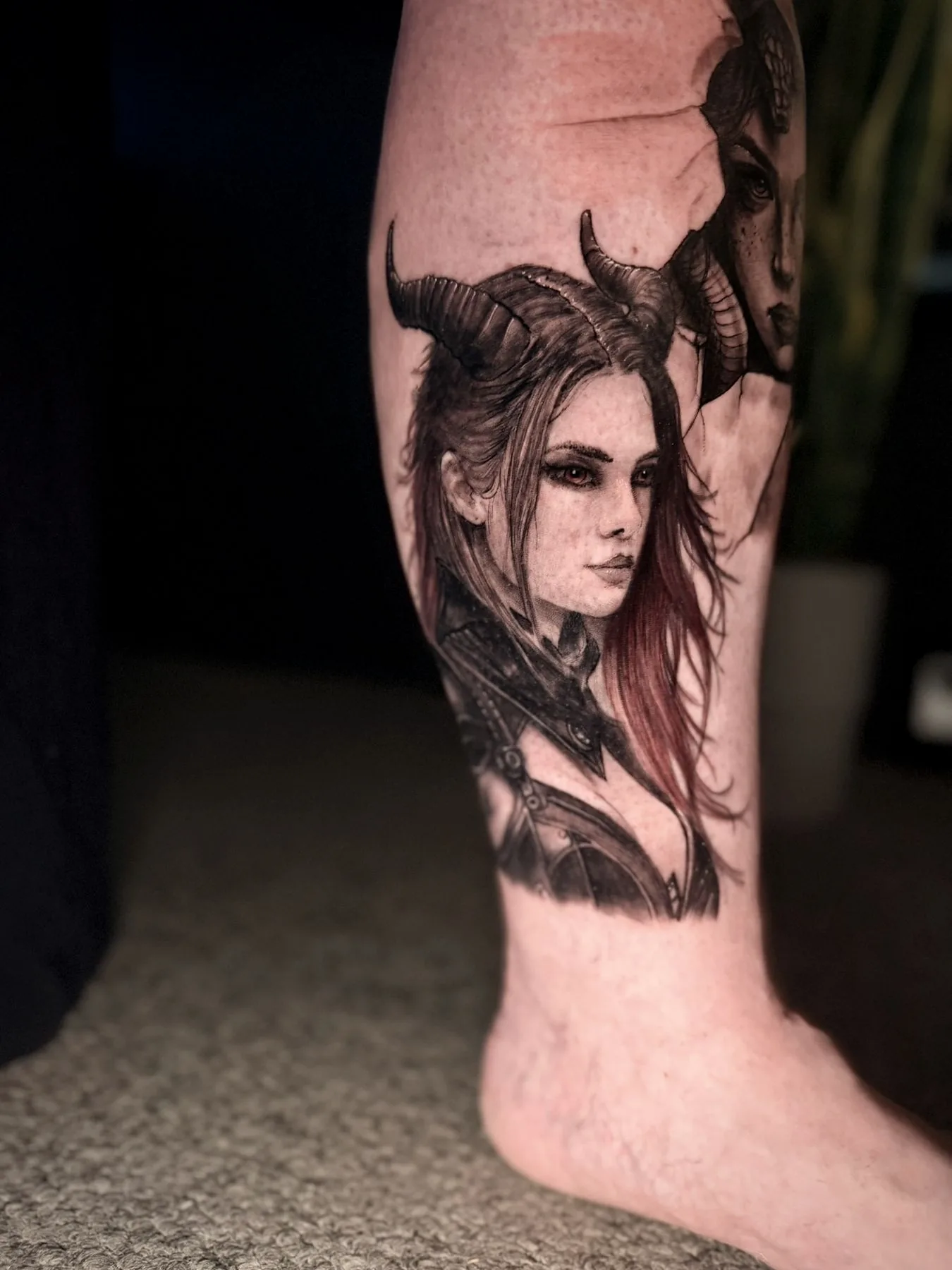 A horned woman's portrait on a forearm, her long hair carrying red through the black and grey.