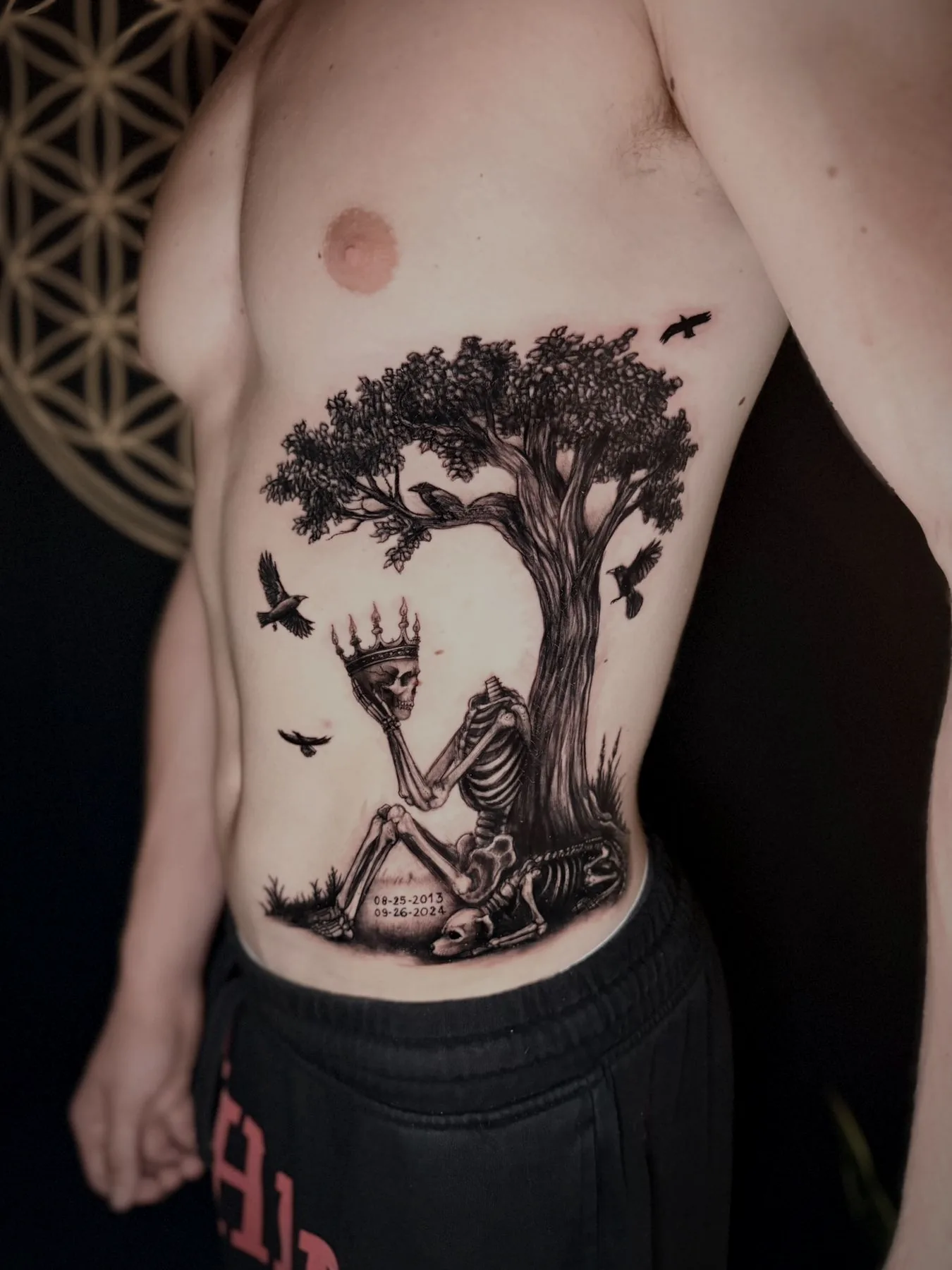 A skeleton seated beneath a bare tree with birds in flight, tattooed across a ribcage.