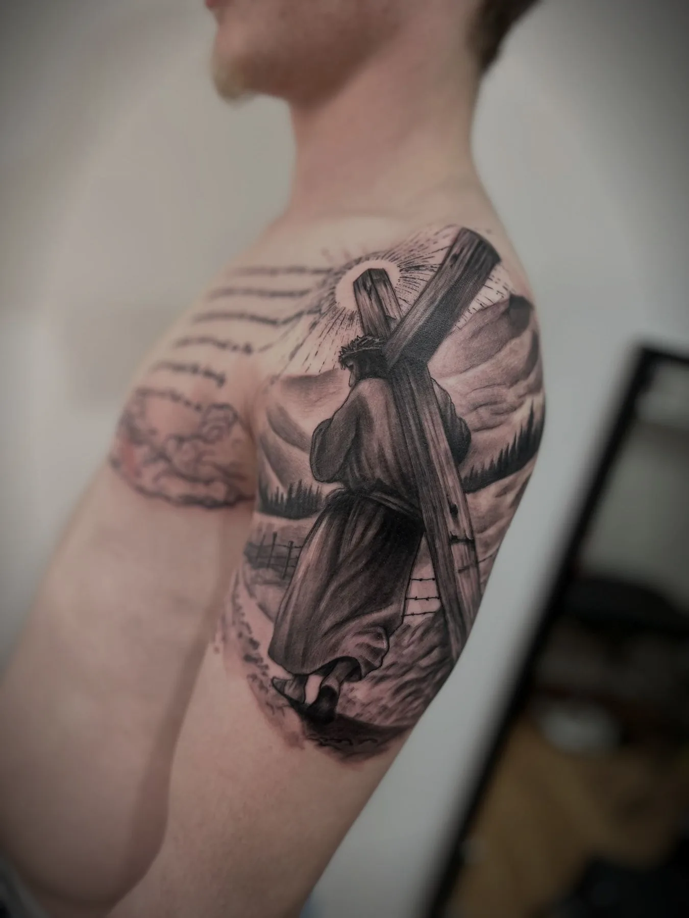 Christ carrying the cross, tattooed across a shoulder beneath a ray of light.