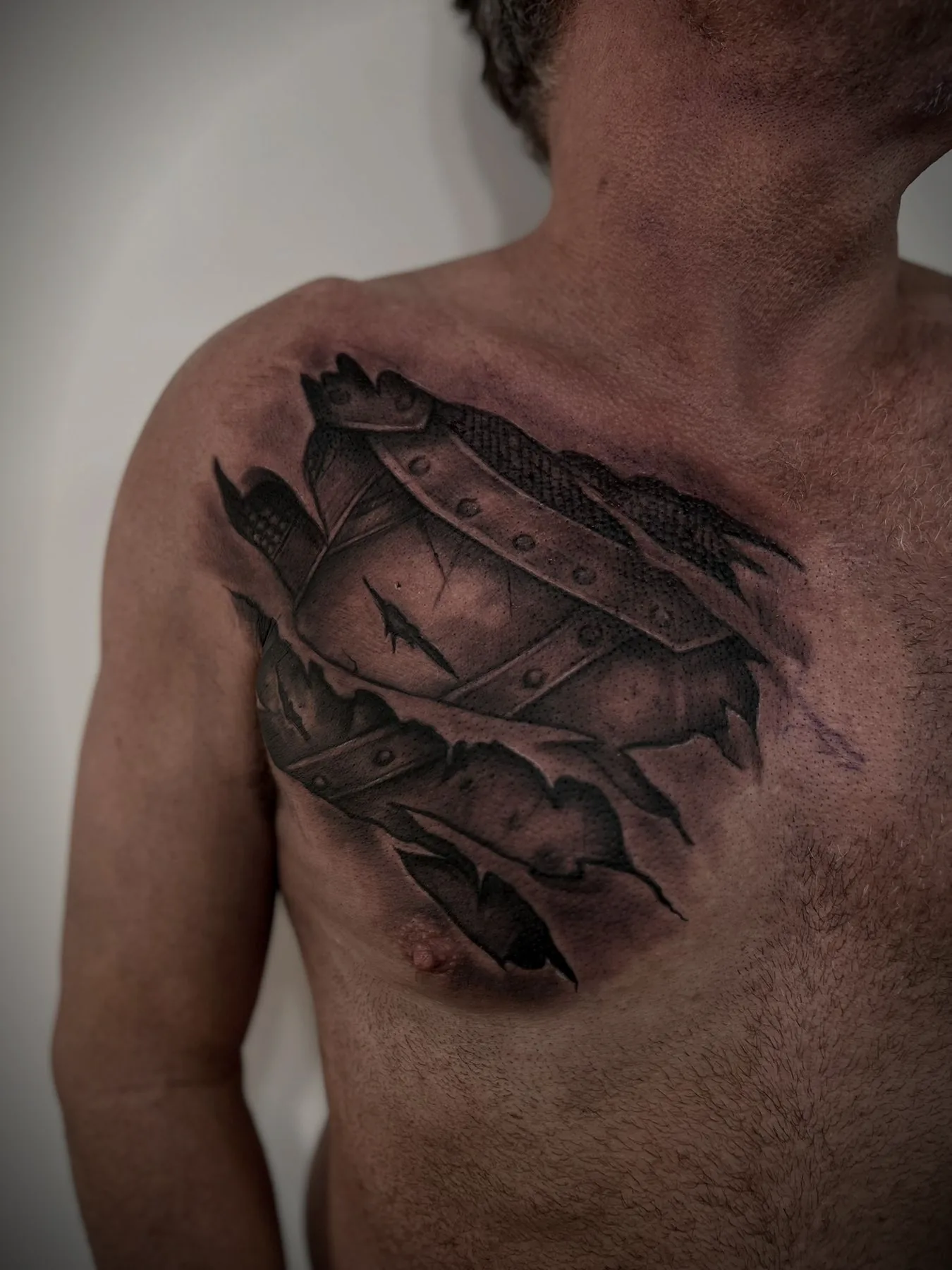 Armour plating torn open across a chest, tattooed to look as though the skin is peeling back.