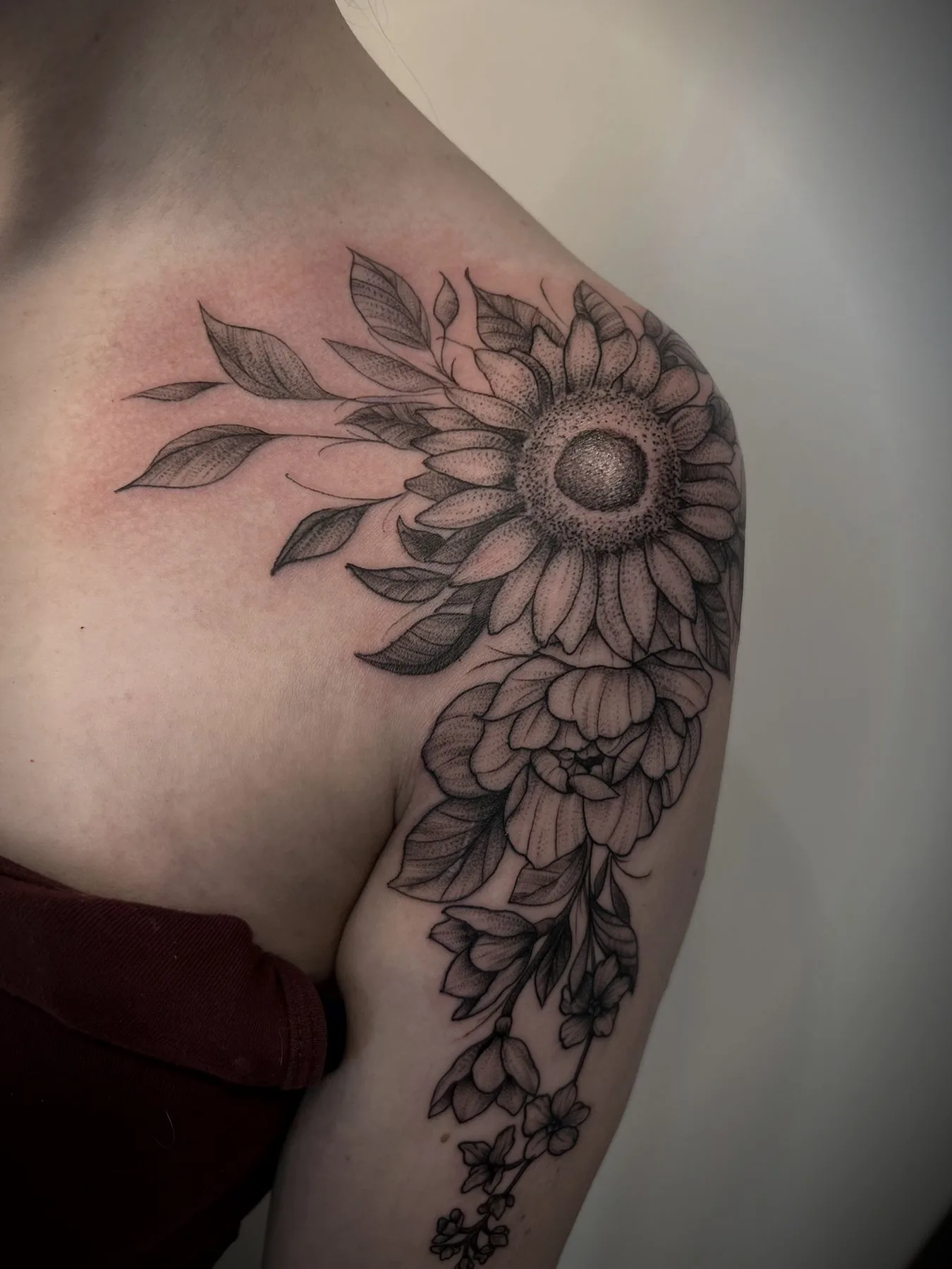 A sunflower and blossoms across a shoulder in fine black linework.