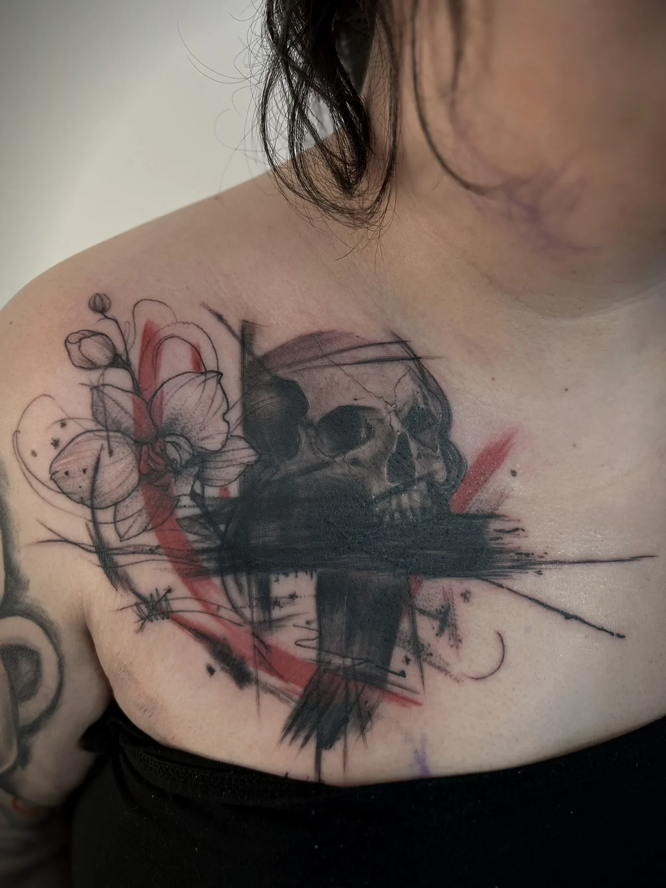 A skull over a black cross, cut through with red brushstrokes, tattooed across a chest.