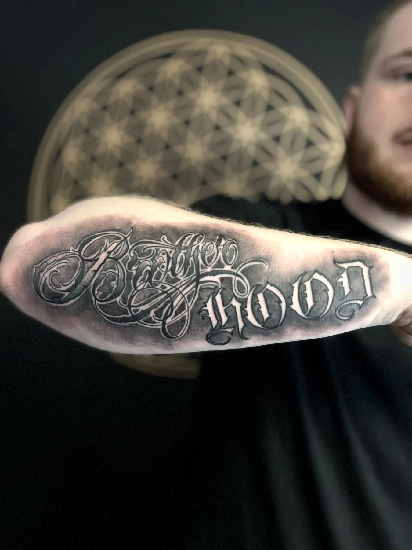 The word 'Brotherhood' tattooed on an inner arm in ornate script.