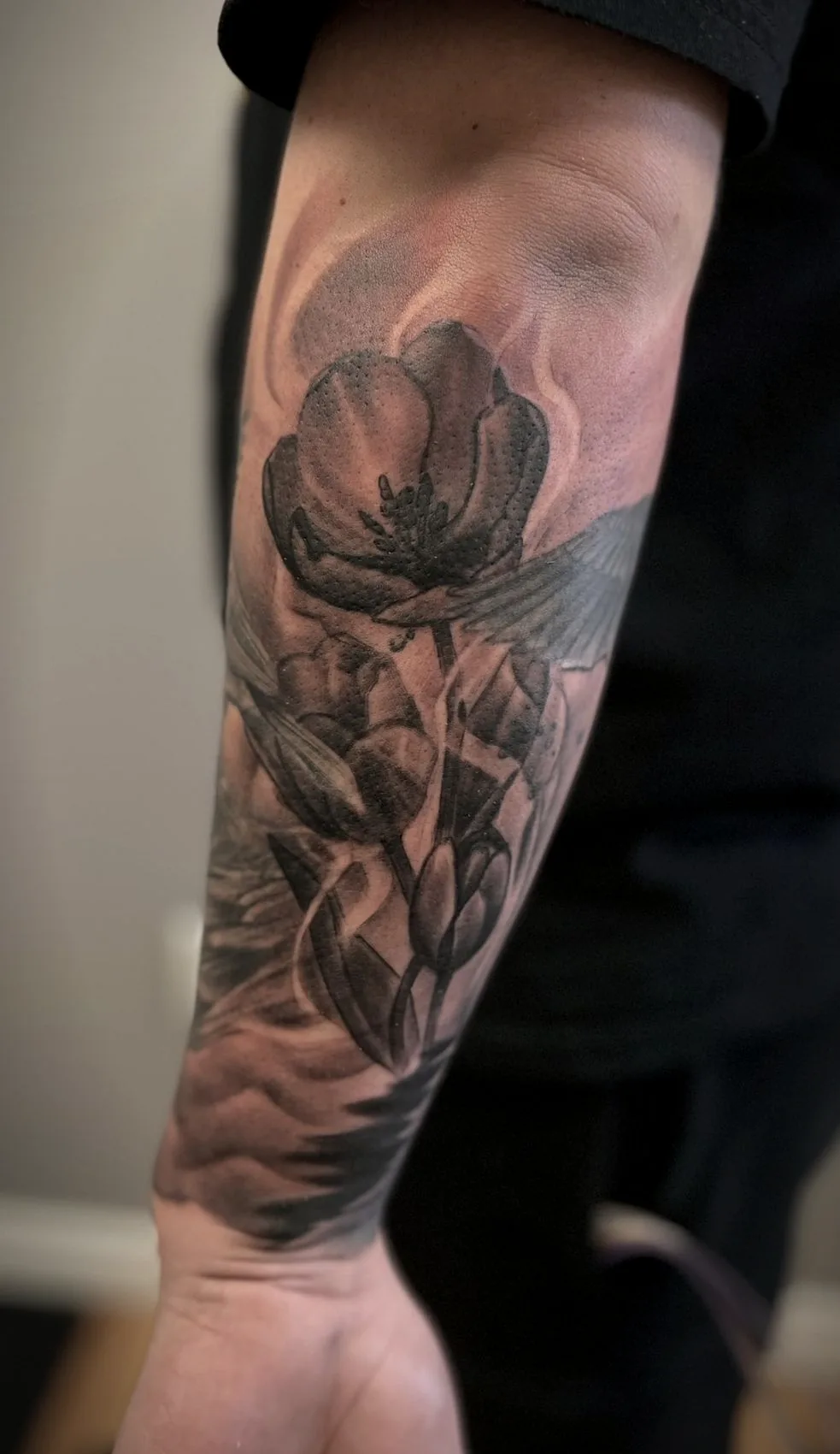 Tulips tattooed along a forearm in soft black and grey, the skin still flushed from the session.