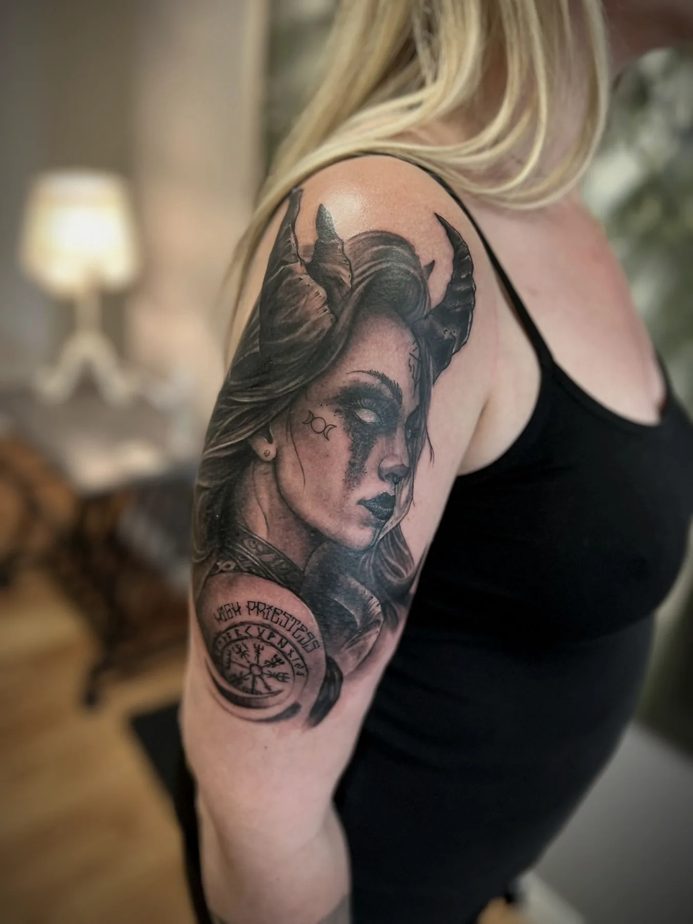 A horned woman's portrait on an upper arm, with a compass rose beneath it.
