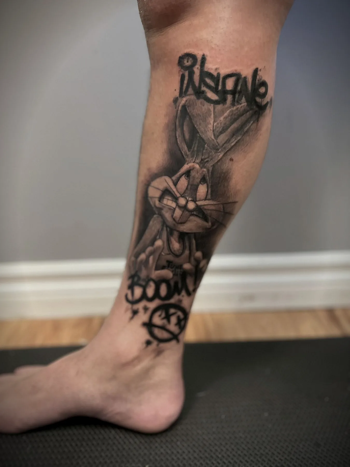 A cartoon rabbit and graffiti lettering tattooed down a shin and ankle.