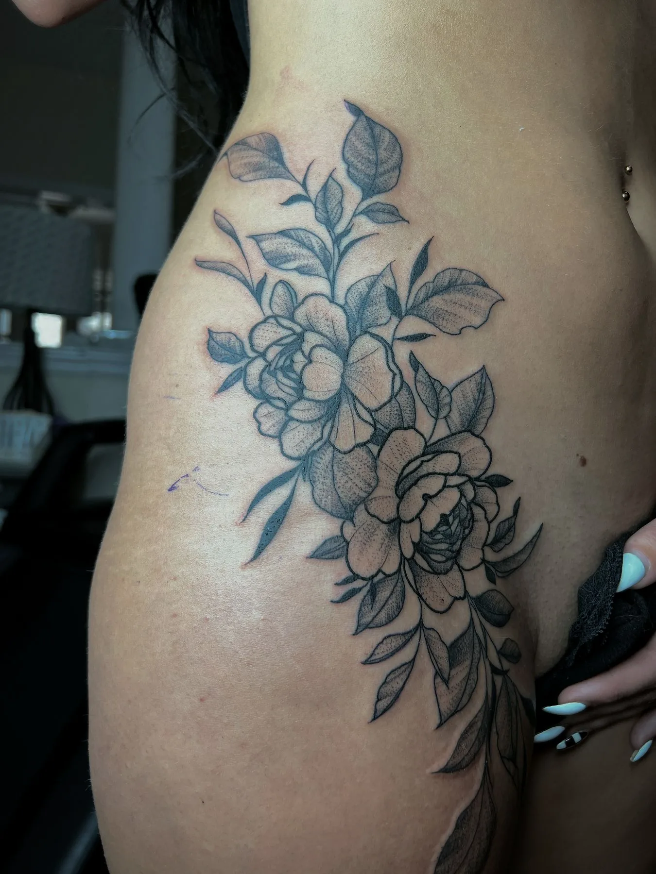 Roses and leaves in blue ink, tattooed down a ribcage and hip.