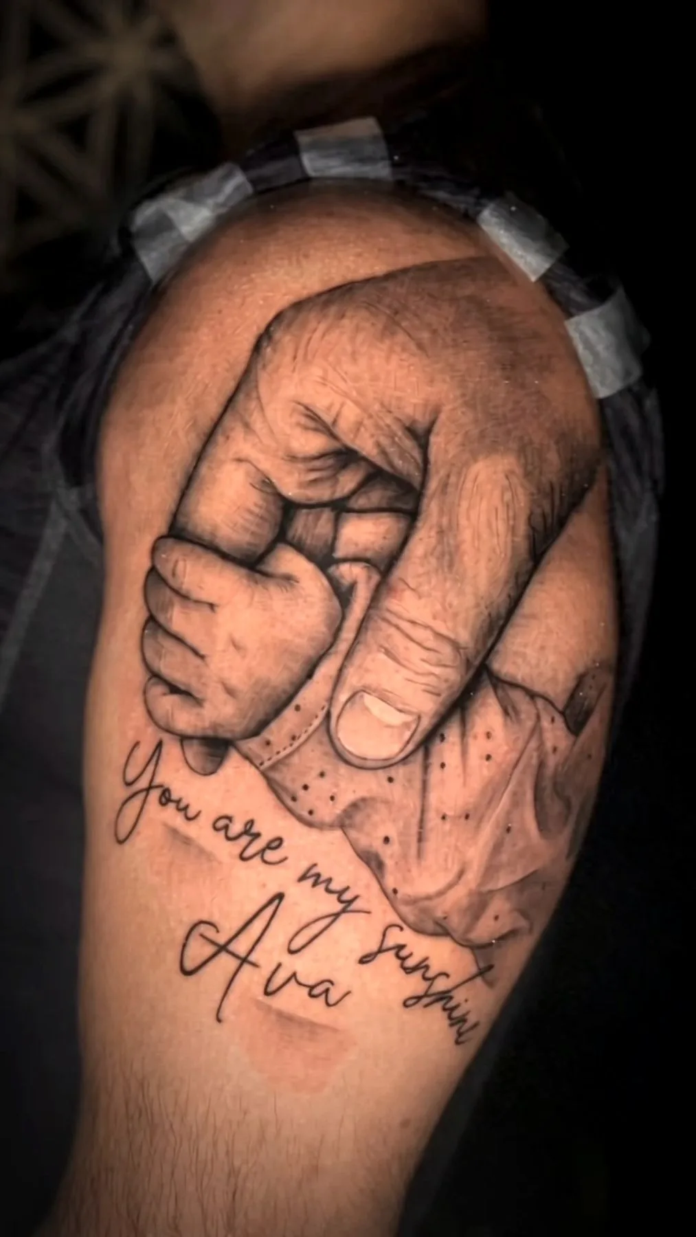 Two hands clasped in a family piece, tattooed on a forearm in black and grey.