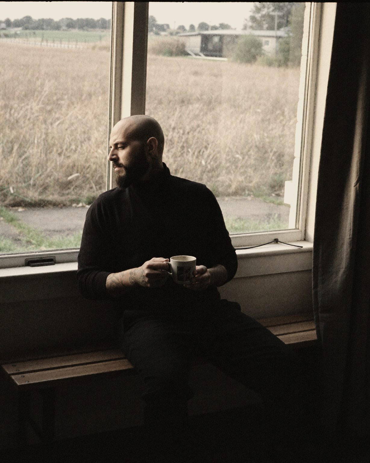 Nicolás Morin sitting by a window with a cup of coffee, a field outside.